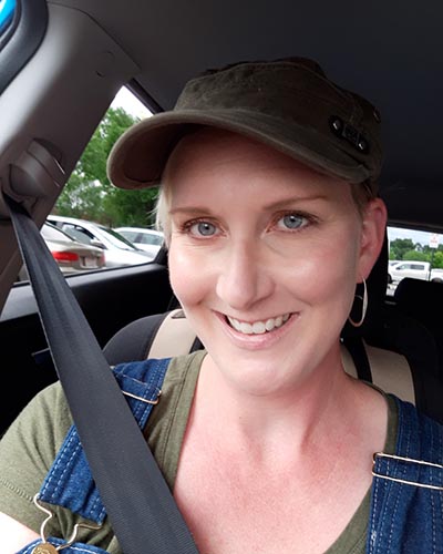 A woman wearing a baseball style hat is smiling while sitting in their car